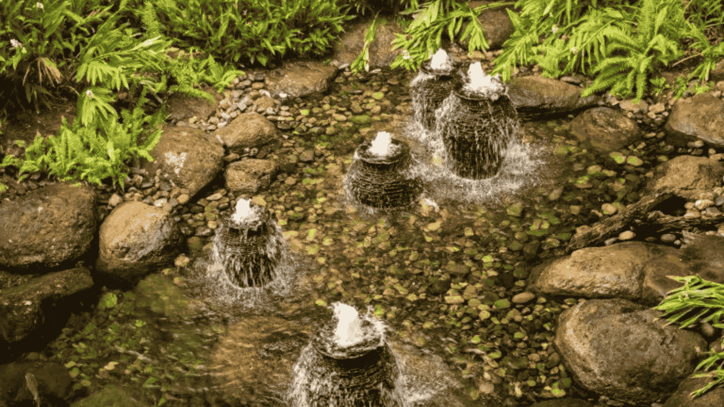 A pond with five vase shaped fountains inside of it.